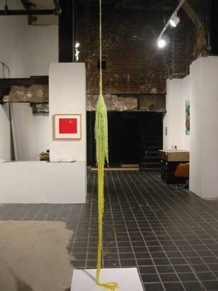 a long, thin, green and yellow crocheted work that hung from the ceiling onto a small table in the middle of the gallery